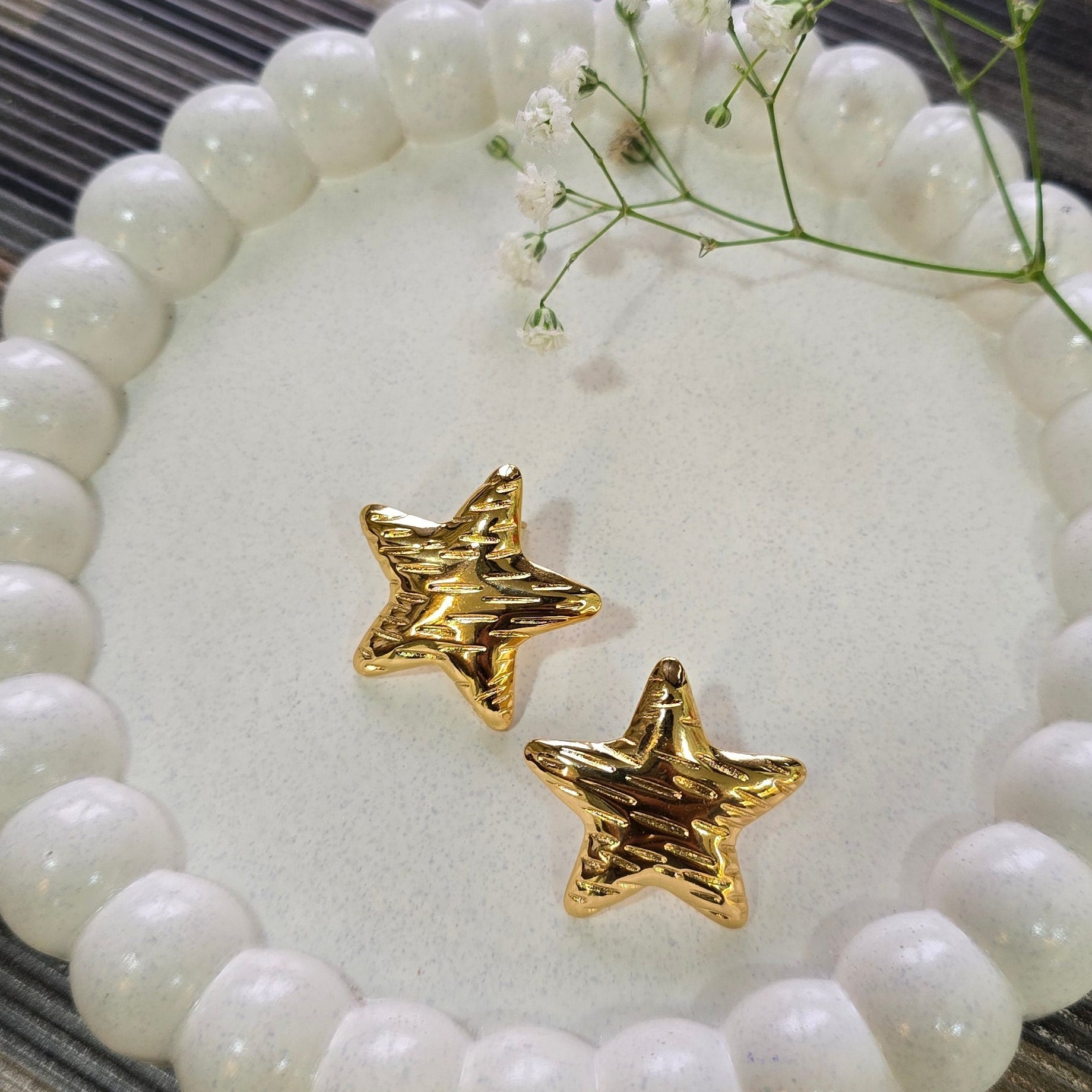 Gold star-shaped earrings on a white beaded dish with flowers on a wooden surface